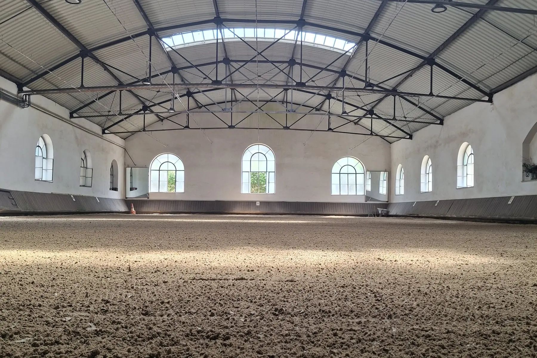 Blick in die Reithalle mit Rundbogenfenstern und frisch abgezogenem Sandboden